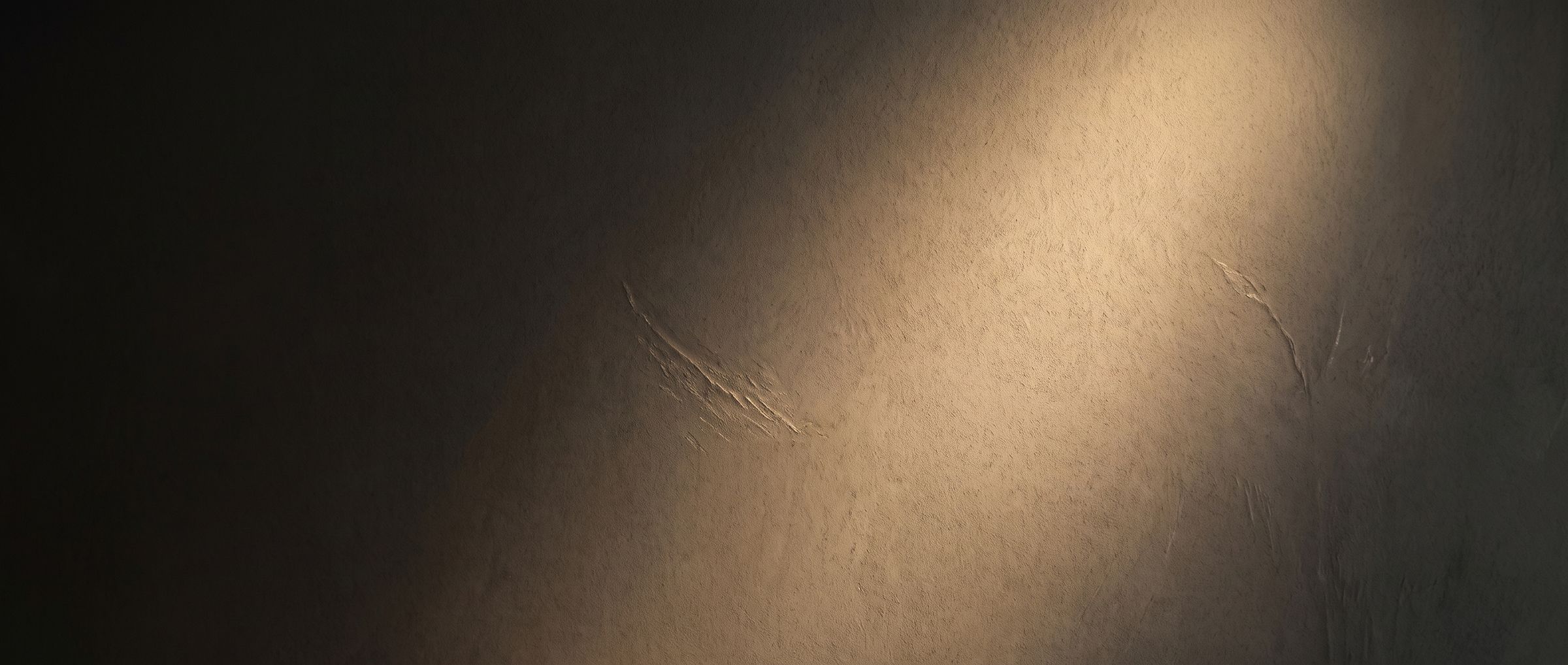 Warm gold light raking across a dark plaster wall